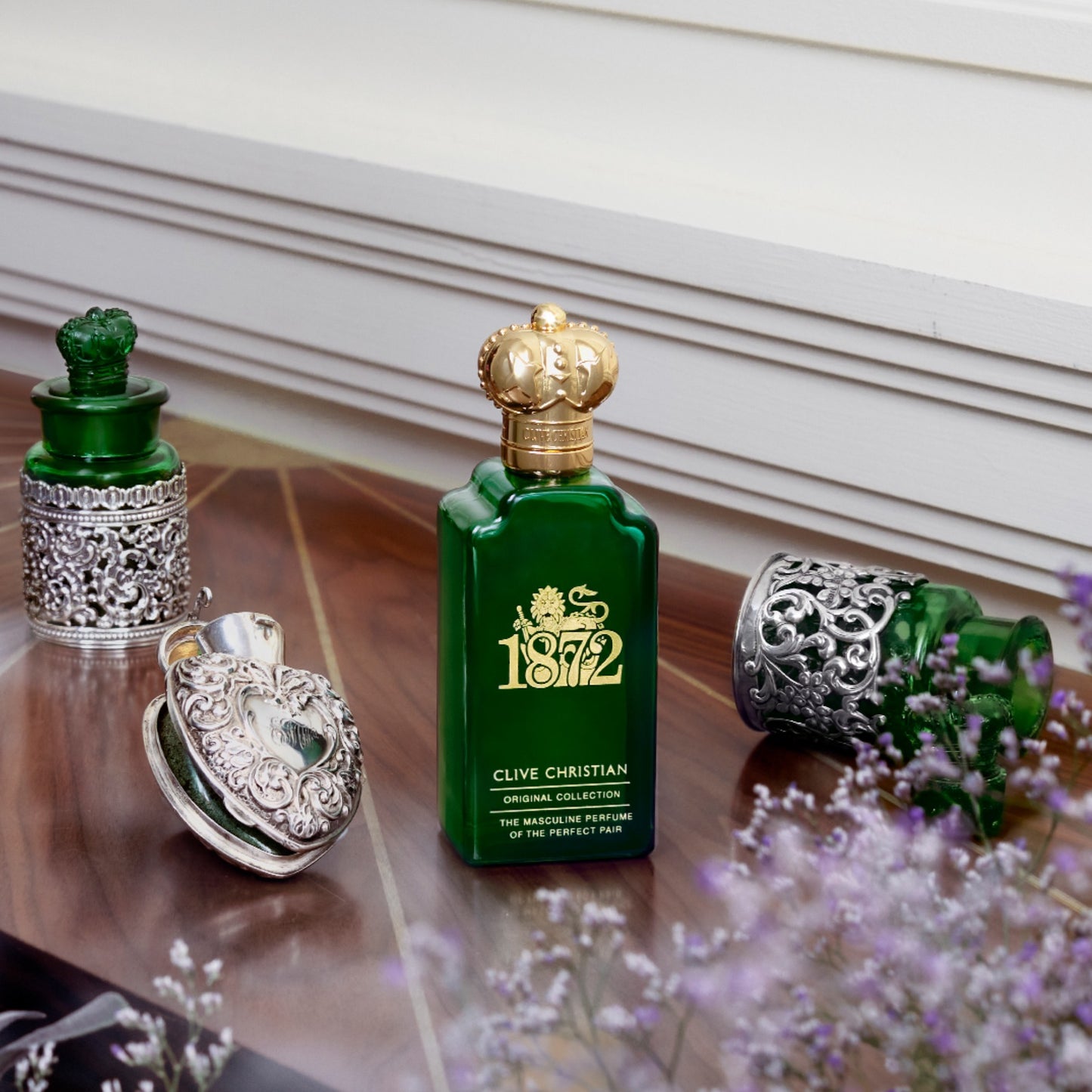 Clive Christian 1872 masculine perfume bottle in its signature green glass with gold accents. The perfume sits on a vanity with decorative antique bottles.