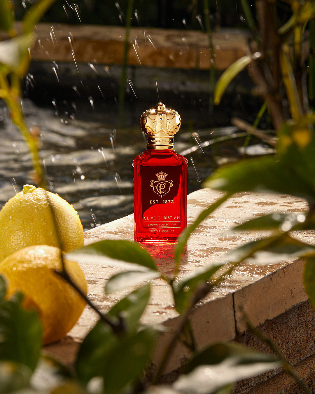 Clive Christian Crown Collection perfume bottle in "Town & Country" scent, displayed outdoors with fresh lemons beside a fountain.
